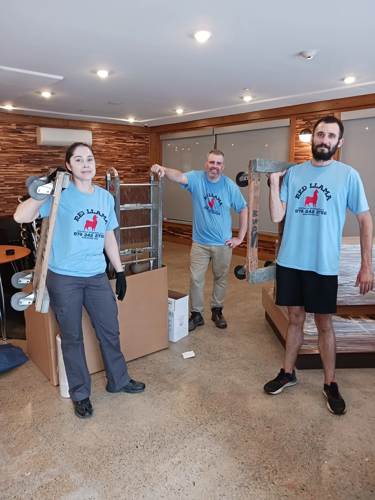 Red Llama moving crew with boxes and a dolly inside a home.